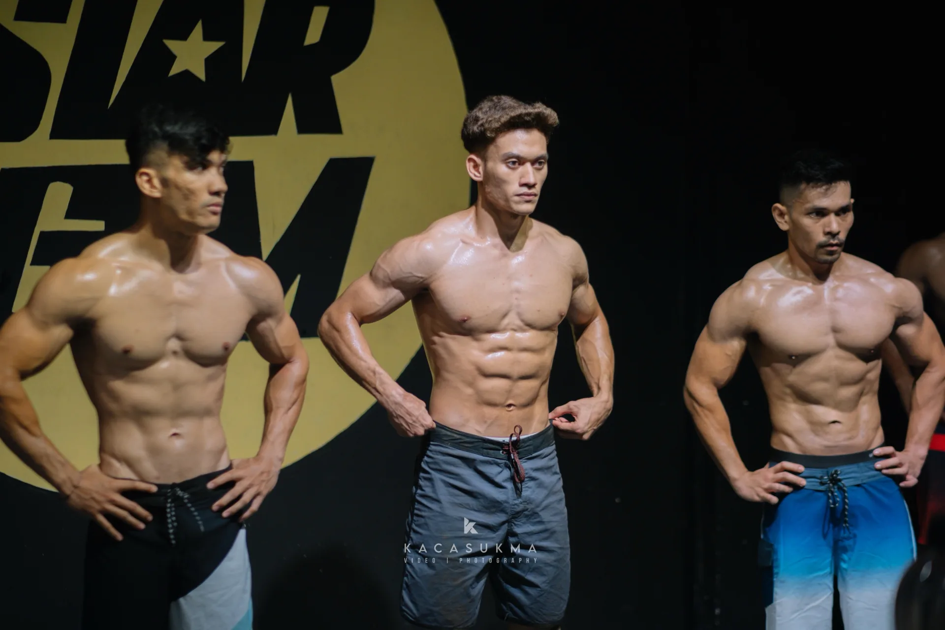 Athletes posing on stage under stage lighting at a Star Gym bodybuilding competition